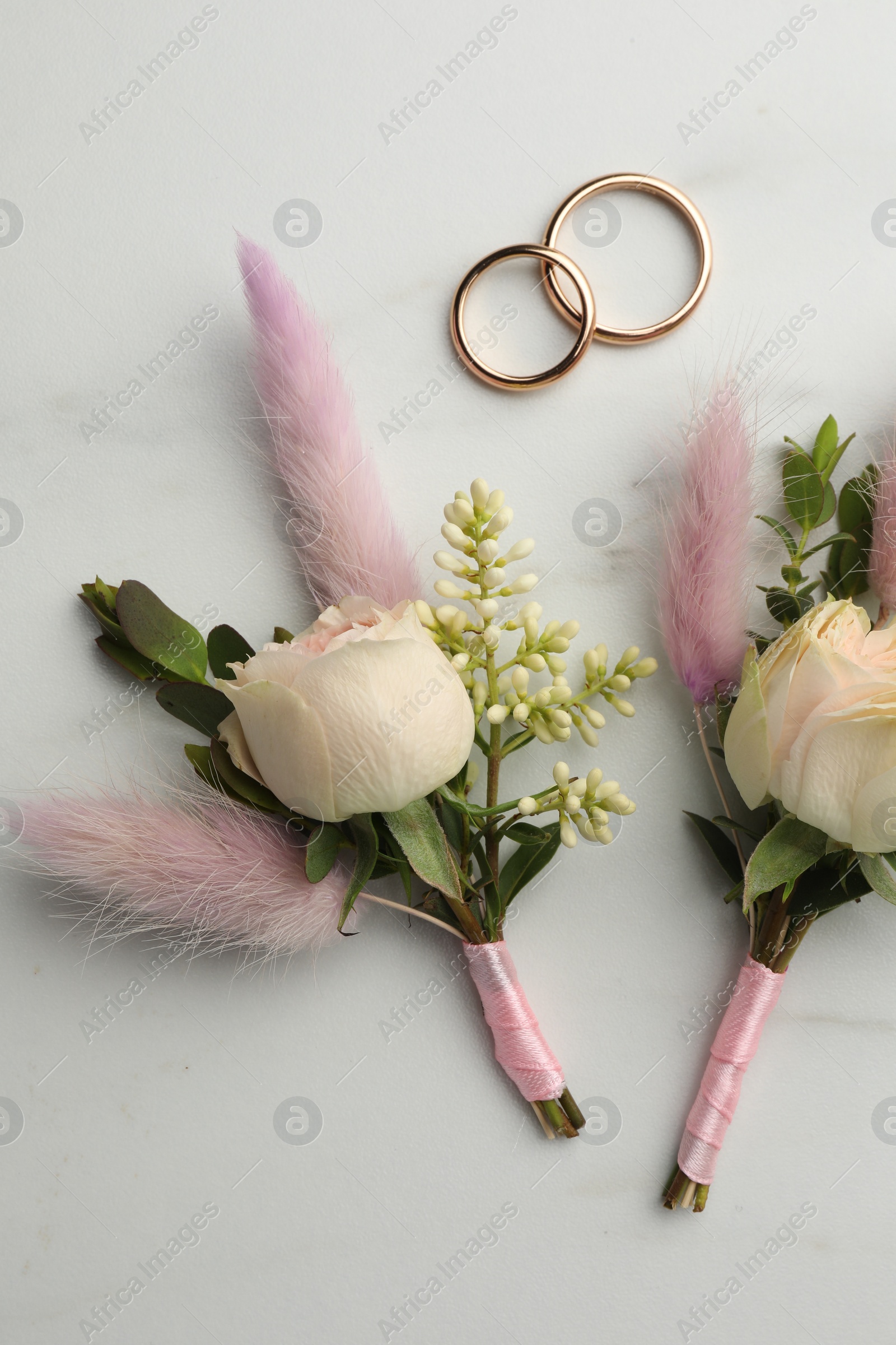 Photo of Small stylish boutonnieres and rings on white marble table, flat lay