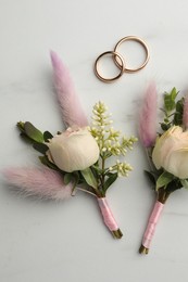 Small stylish boutonnieres and rings on white marble table, flat lay