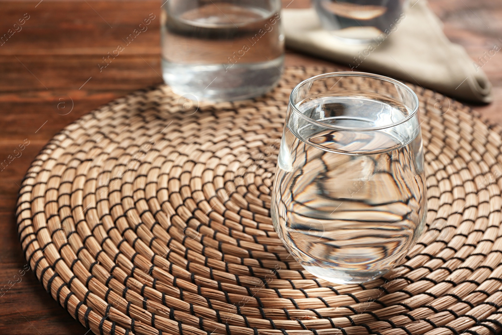 Photo of Glass with fresh water and bamboo mat on wooden table. Space for text