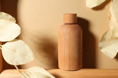 Photo of Wooden bottle of cosmetic product and dried leaves on dark beige background