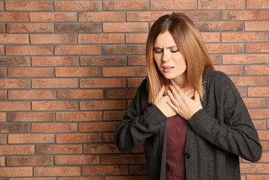 Photo of Woman suffering from cough near brick wall. Space for text