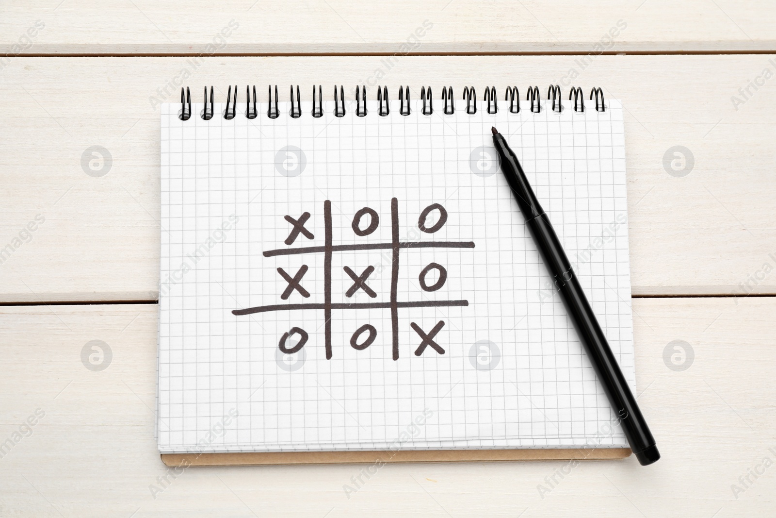 Photo of Notebook with tic tac toe game and marker on white wooden table, top view