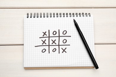 Notebook with tic tac toe game and marker on white wooden table, top view