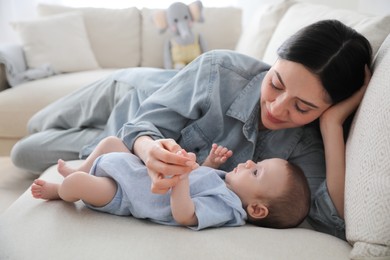 Photo of Young woman with her cute baby on sofa at home