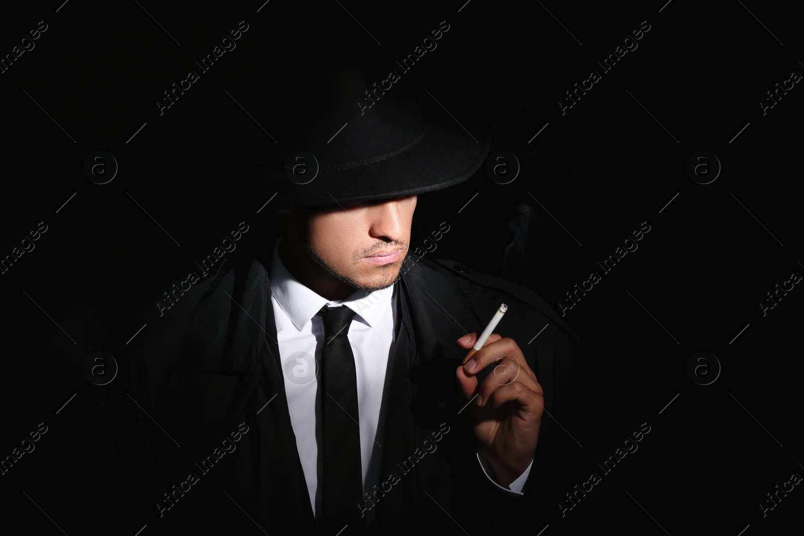 Photo of Old fashioned detective smoking cigarette on dark background