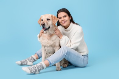 Happy woman playing with cute Labrador Retriever on light blue background