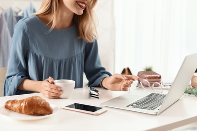 Photo of Female blogger with laptop and cup of coffee at table indoors, closeup. Online broadcast