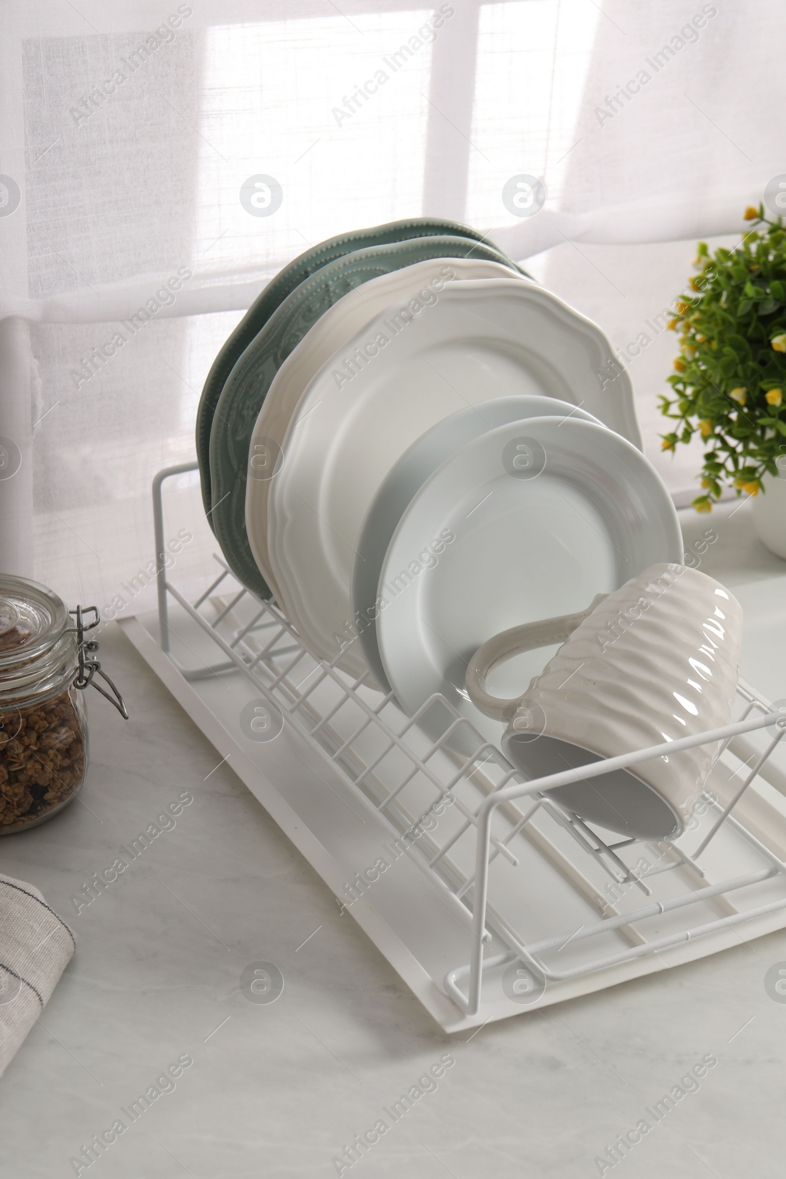 Photo of Drainer with different clean dishware and cup on light table indoors