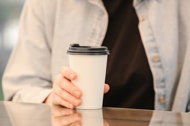 Woman holding takeaway paper cup at table, closeup. Coffee to go