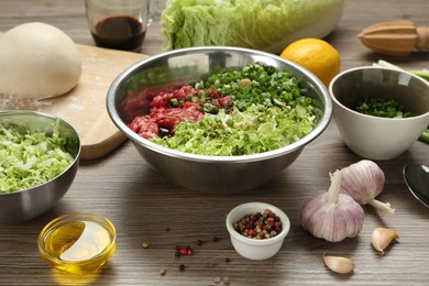 Photo of Bowl with gyoza filling, raw dough and ingredients on wooden table