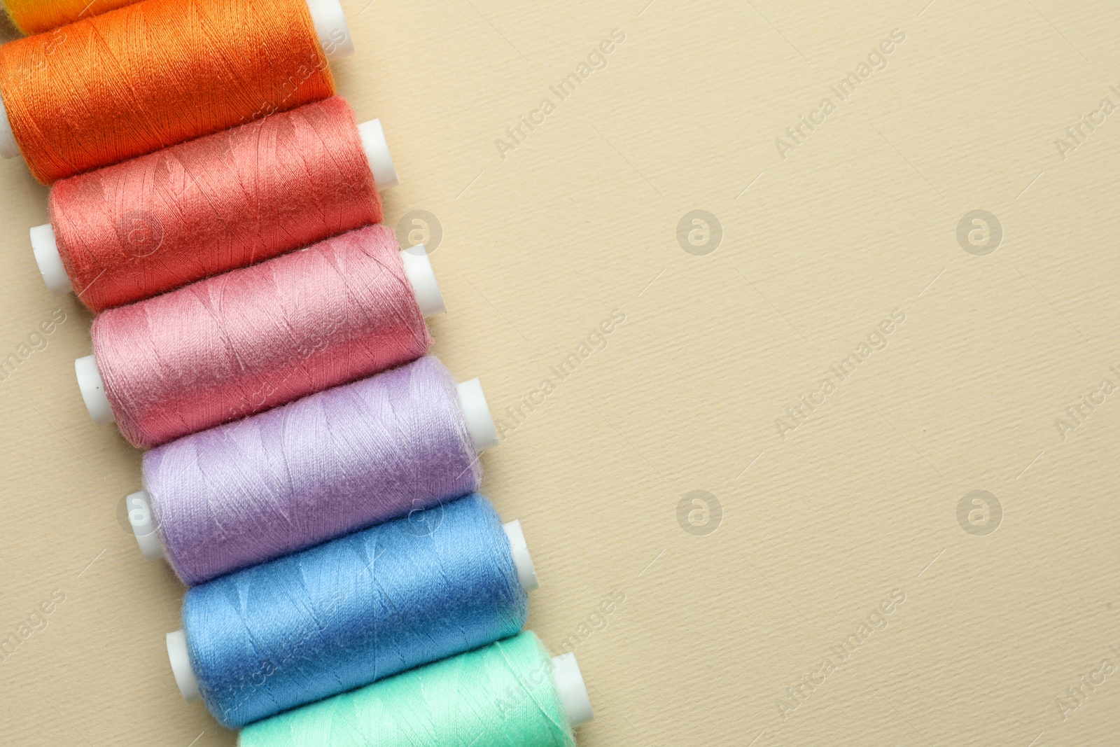 Photo of Set of colorful sewing threads on beige background, flat lay. Space for text