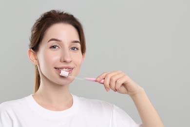 Photo of Smiling woman with dental braces cleaning teeth on grey background. Space for text