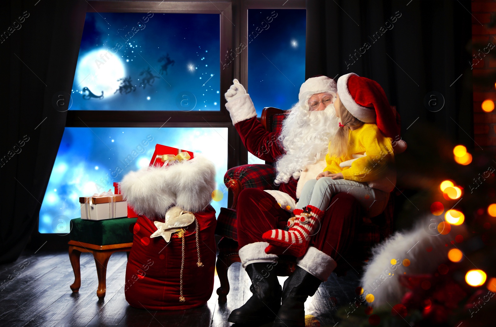 Image of Santa Claus with little girl in armchair at home. Christmas time