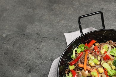 Stir fried noodles with mushrooms and vegetables in wok on grey table, top view. Space for text