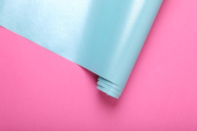 Roll of wrapping paper on pink background, top view