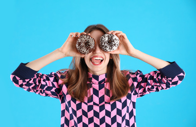 Beautiful young woman with donuts on light blue background