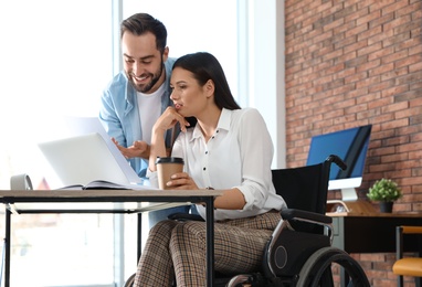 Photo of Young woman in wheelchair with colleague at workplace