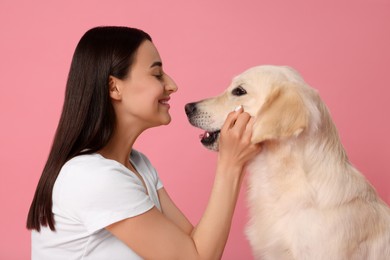 Happy woman playing with cute Labrador Retriever dog on pink background. Adorable pet