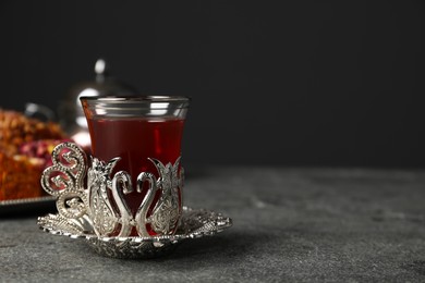 Photo of Glass of traditional Turkish tea in vintage holder on grey table, space for text