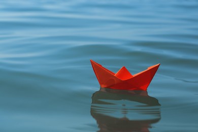 Photo of Orange paper boat floating on water surface, space for text