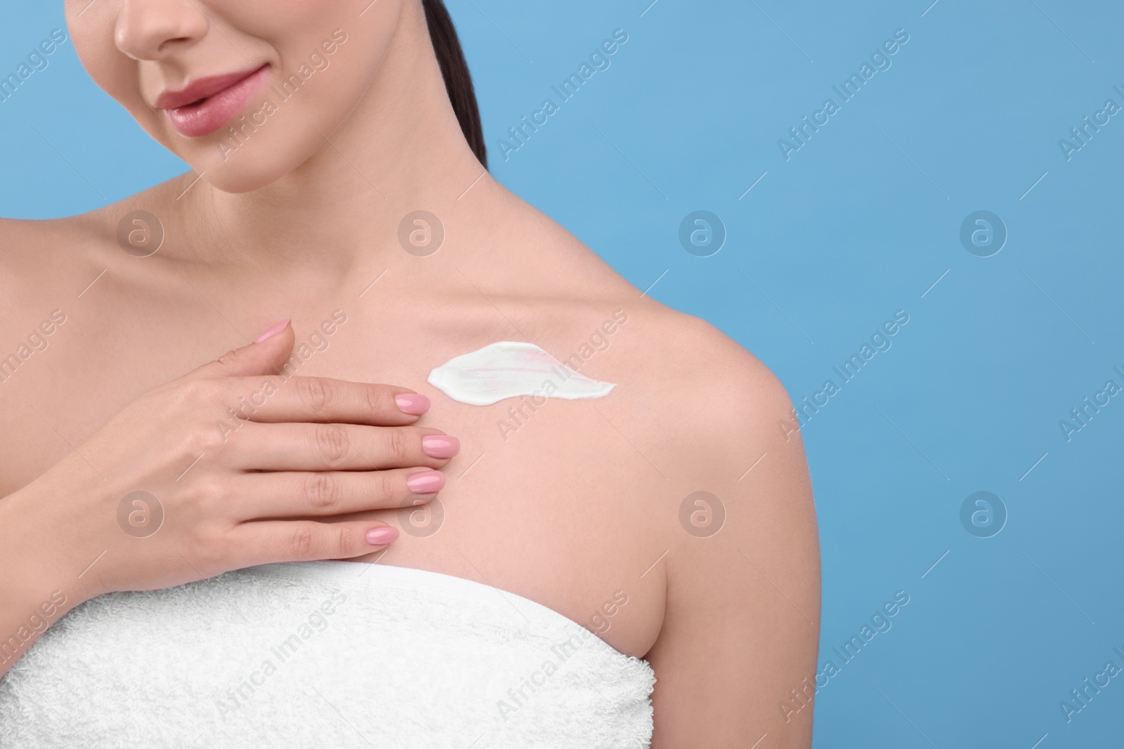 Photo of Woman with smear of body cream on light blue background, closeup. Space for text