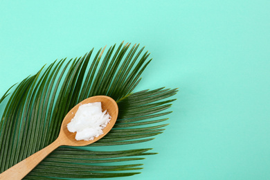 Organic coconut oil and palm branch on turquoise background, top view. Healthy cooking