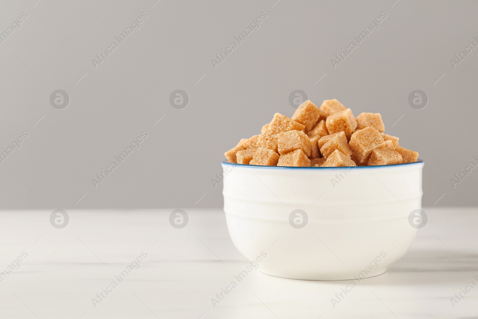 Photo of Brown sugar cubes in bowl on white table, space for text