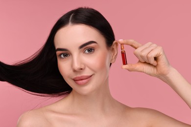 Photo of Beautiful young woman with long healthy hair holding ampoule on pink background