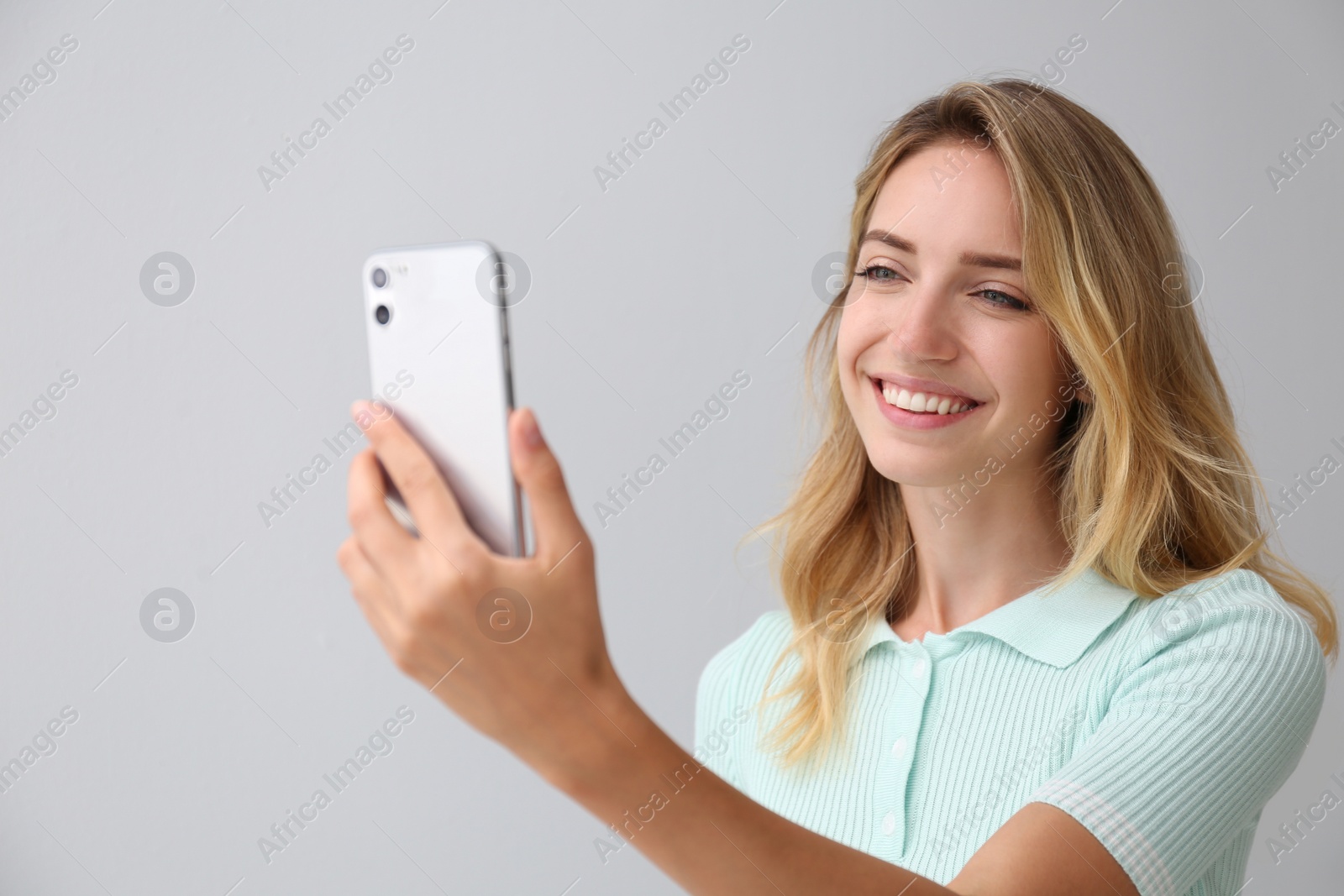 Photo of Young woman unlocking smartphone with facial scanner on grey background. Biometric verification