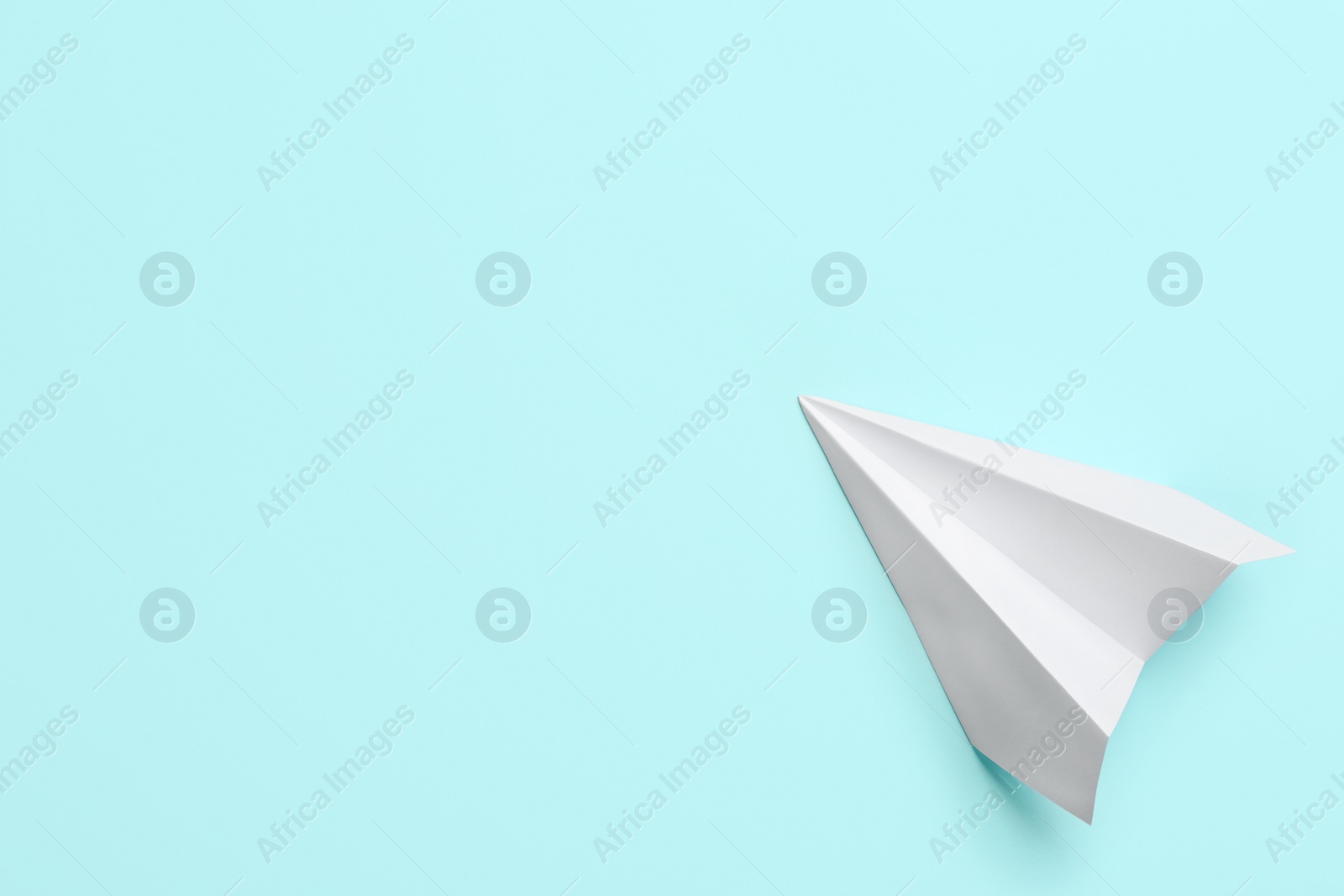 Photo of White paper plane on light blue background, top view. Space for text