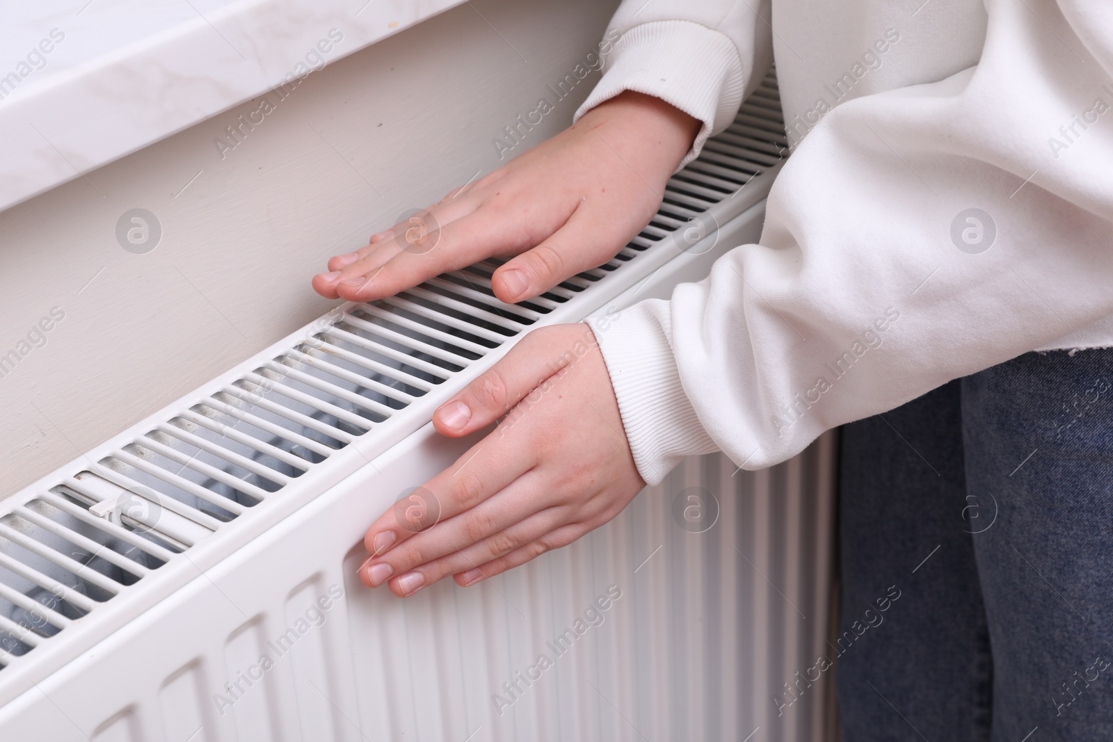 Photo of Girl warming hands on heating radiator indoors, closeup