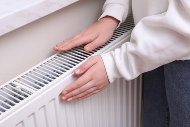 Photo of Girl warming hands on heating radiator indoors, closeup