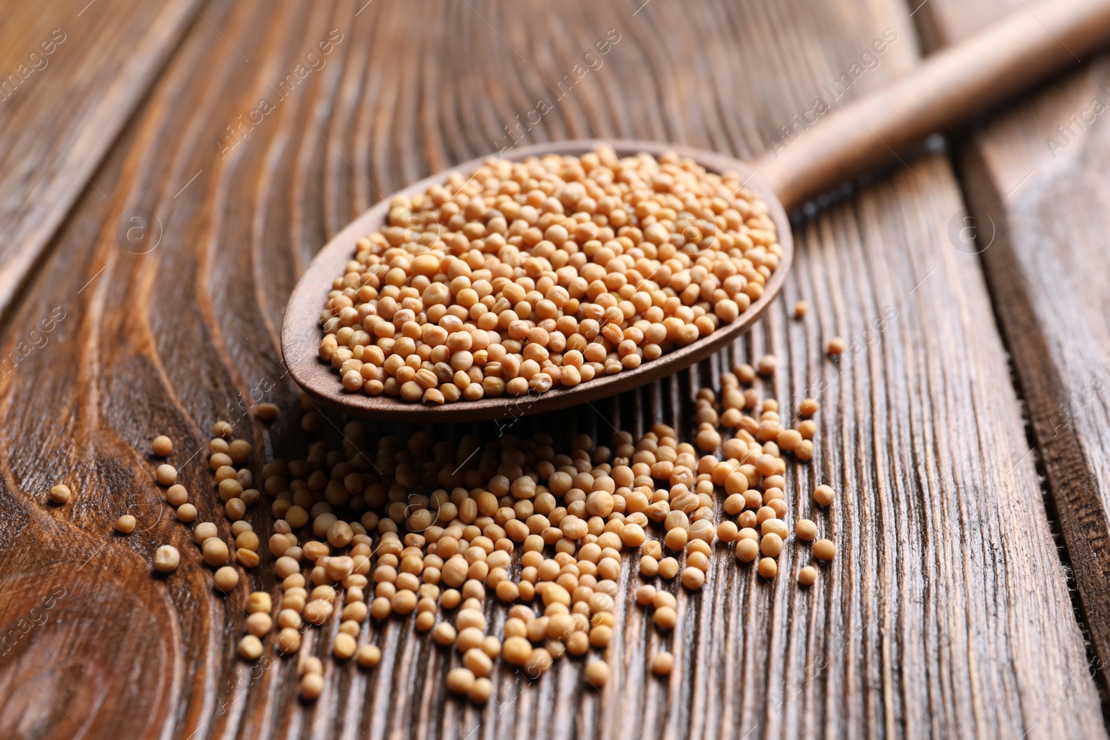 Photo of Mustard seeds and spoon on wooden table, closeup