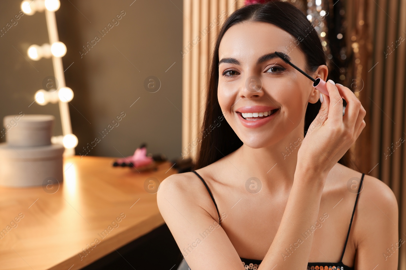 Photo of Beautiful young woman applying mascara in dressing room