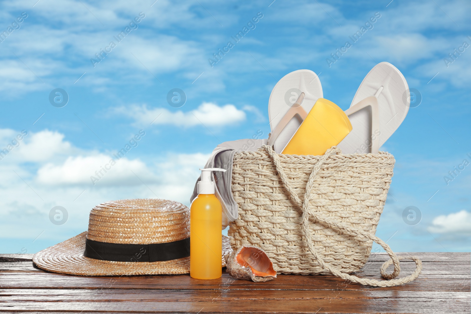 Image of Stylish bag and other beach accessories on wooden table against blue sky