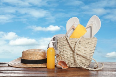 Image of Stylish bag and other beach accessories on wooden table against blue sky