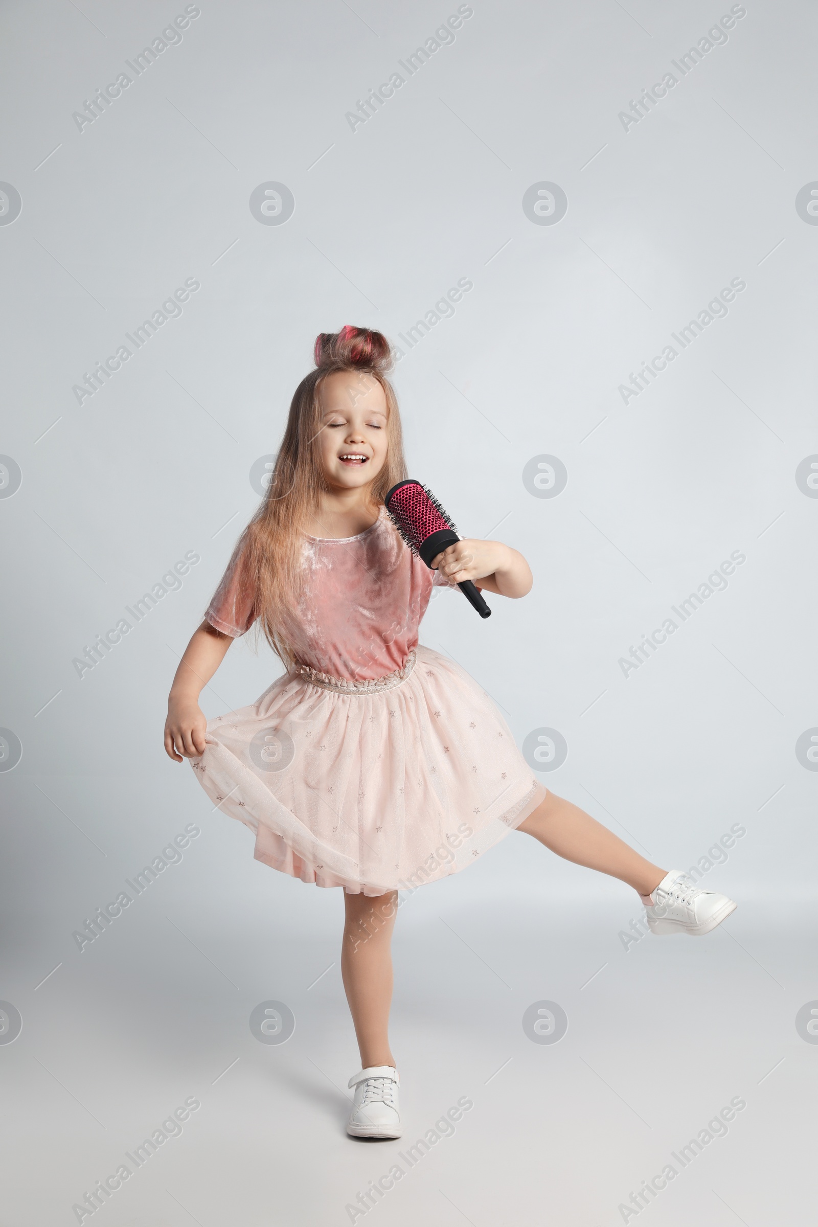 Photo of Cute little girl with hairbrush singing on light grey background