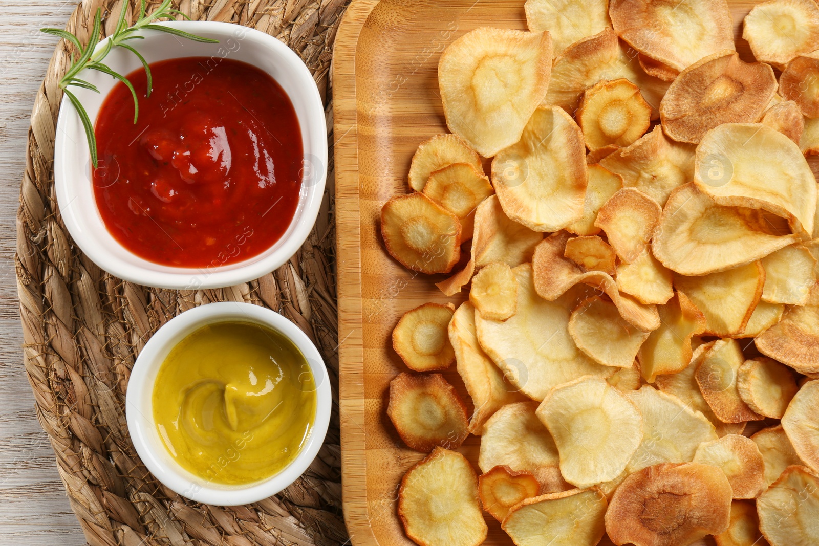 Photo of Tasty homemade parsnip chips with different sauces on wooden table, flat lay