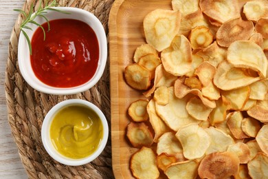 Photo of Tasty homemade parsnip chips with different sauces on wooden table, flat lay
