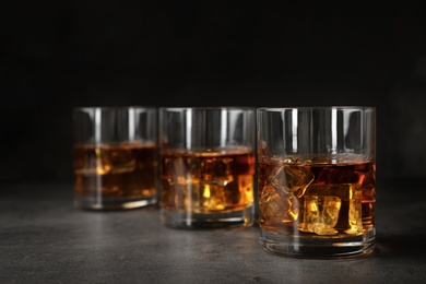 Photo of Golden whiskey in glasses with ice cubes on table. Space for text