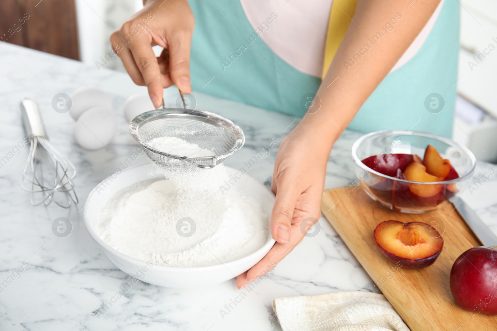 Photo of Woman sieving flour at white marble table, closeup. Cooking of delicious plum cake