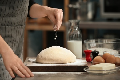 Woman sprinkling flour over dough on table in kitchen