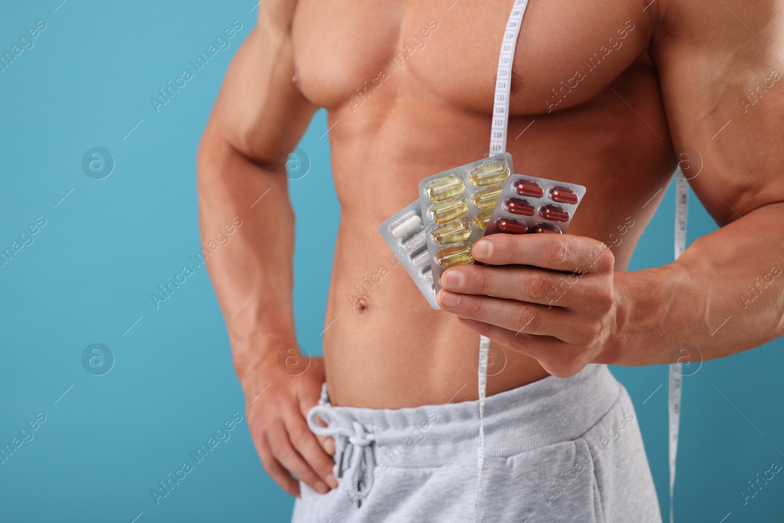 Photo of Weight loss. Athletic man with measuring tape and pills on light blue background, closeup. Space for text