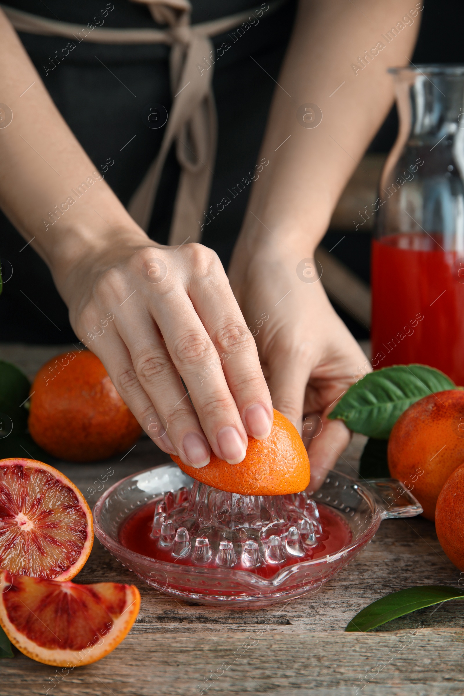 Photo of Woman squeezing sicilian orange juice at wooden table, closeup