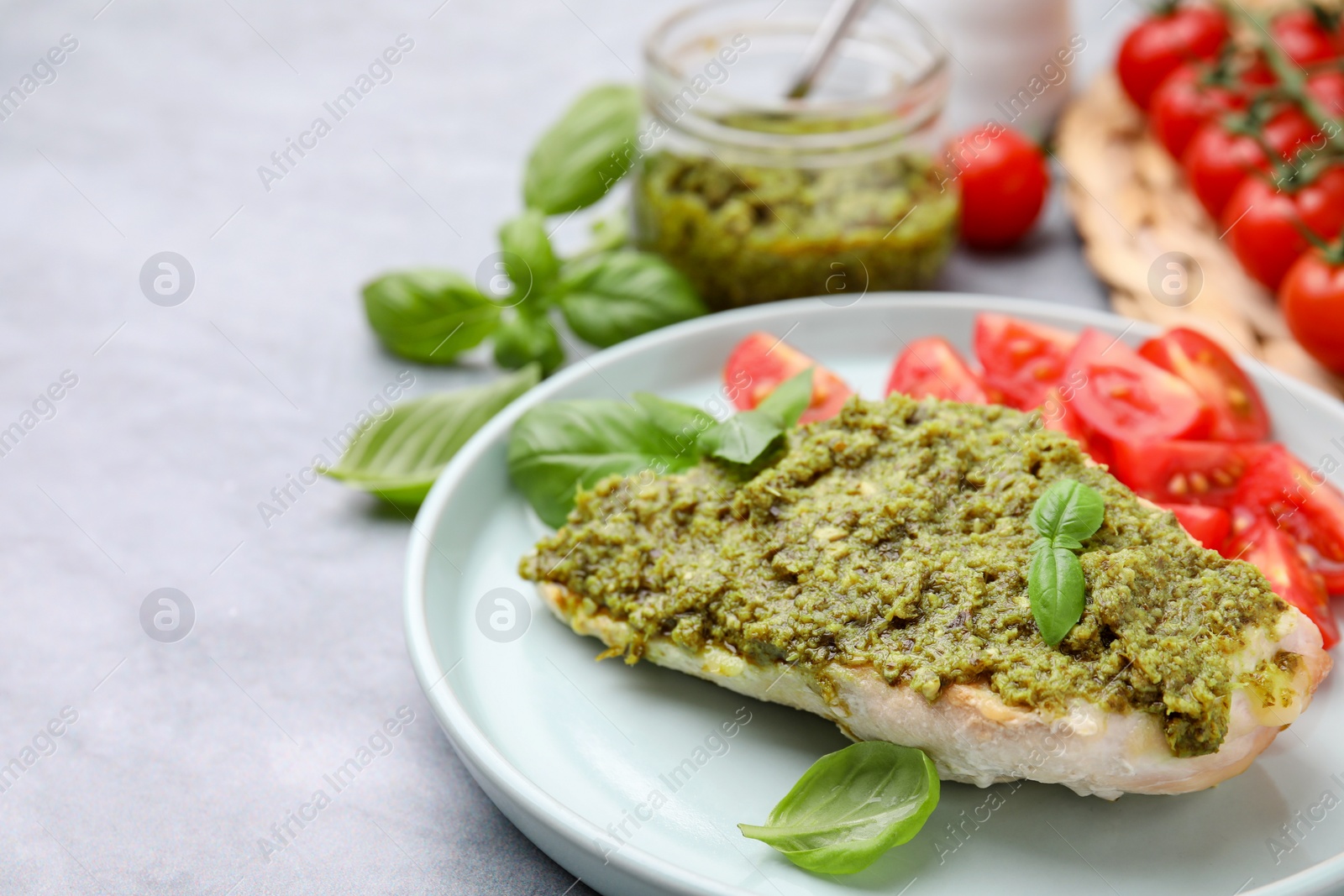 Photo of Delicious chicken breast with pesto sauce and basil on light gray table, closeup. Space for text