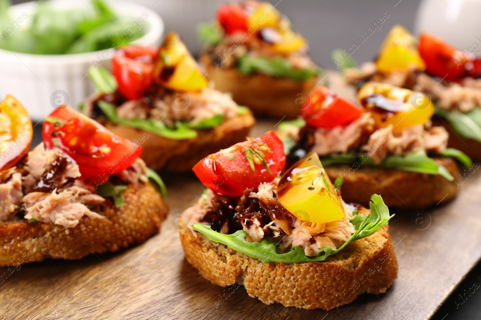 Photo of Delicious bruschettas with balsamic vinegar, tomatoes, arugula and tuna on wooden table, closeup