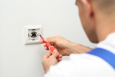 Professional electrician with screwdriver repairing light switch, closeup