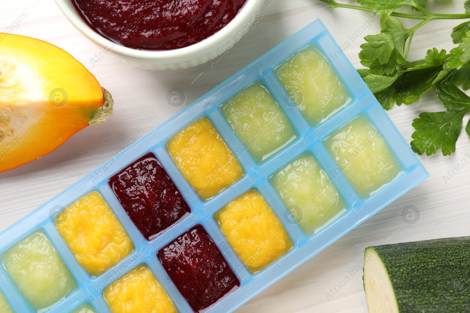 Photo of Different purees in ice cube tray and ingredients on white table, flat lay. Ready for freezing