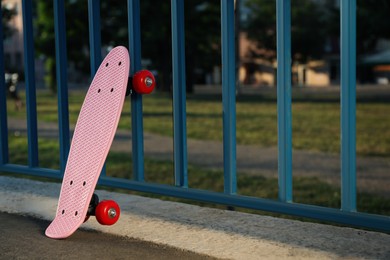 Photo of Modern pink skateboard near fence outdoors. Space for text