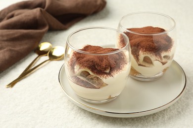 Delicious tiramisu in glasses and spoons on white table